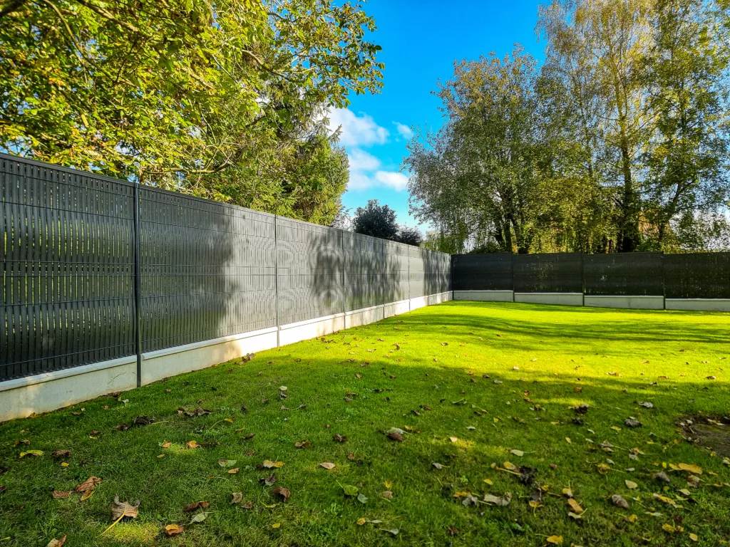 Clôture en acier sombre entourant un jardin verdoyant avec ciel bleu falize et blondel